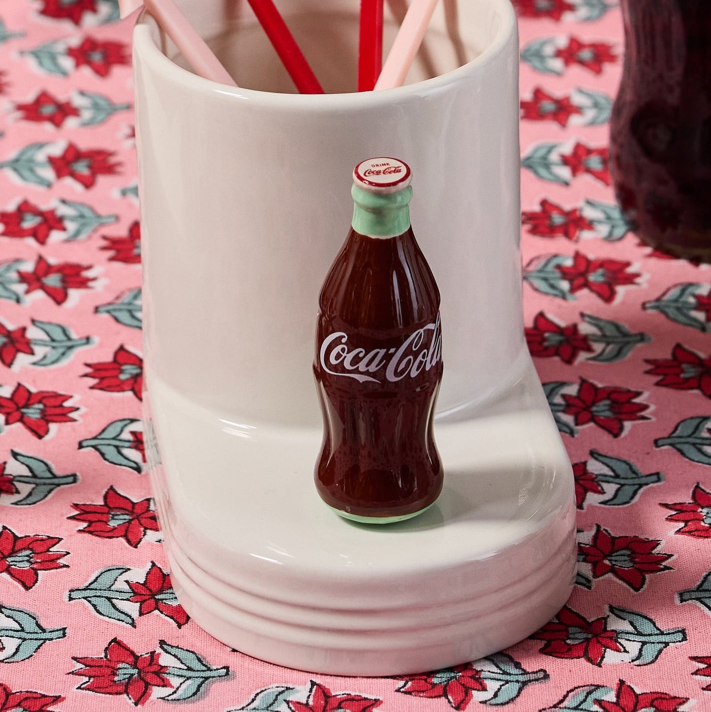 Coca-Cola-themed cup with straw holder on a patterned tablecloth