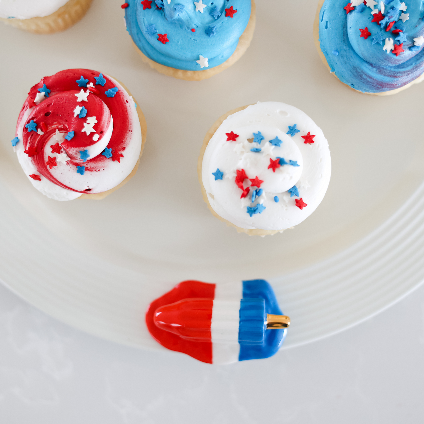 red, white, and blue popsicle and patriotic cupcakes on a round pinstripes platter