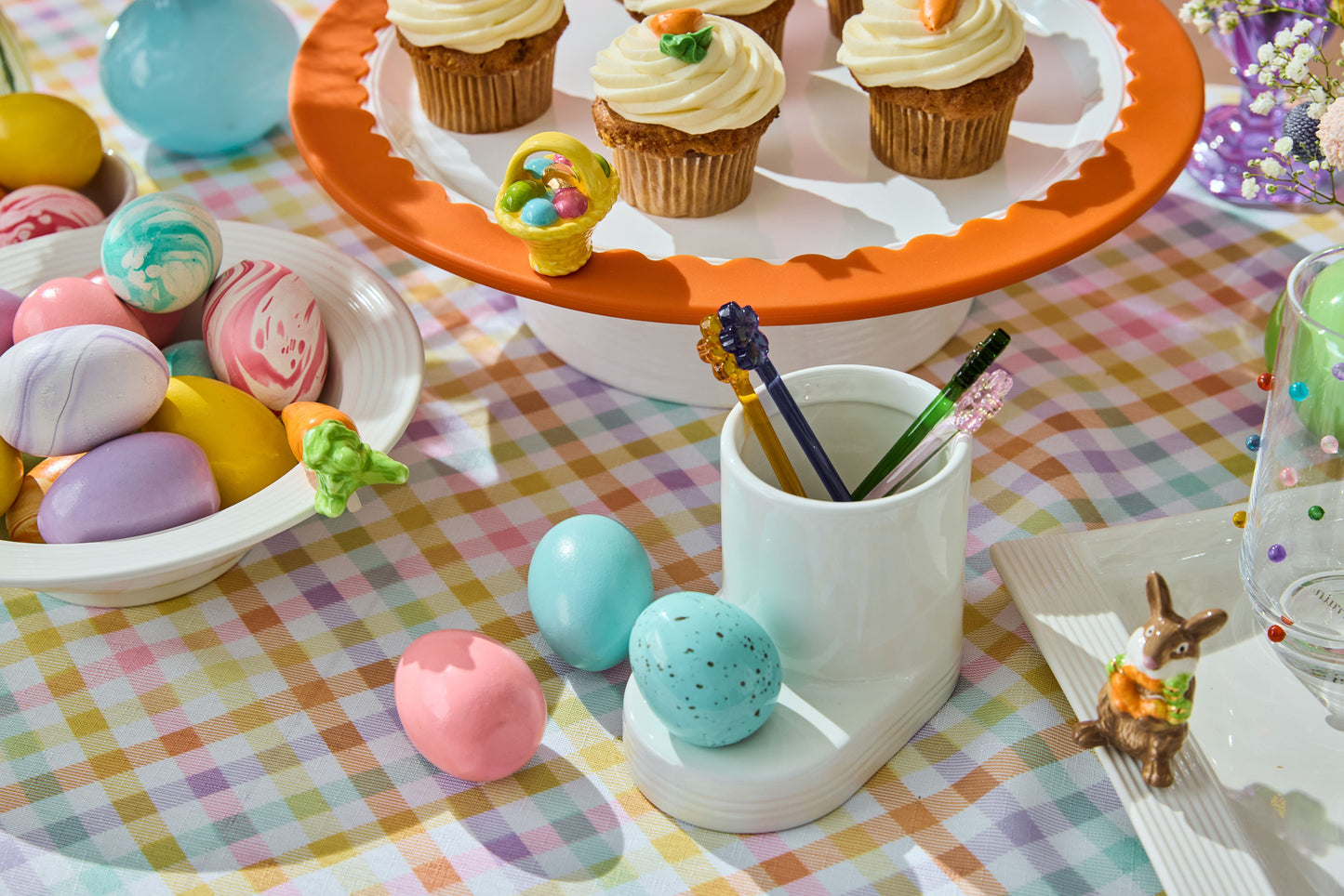 robbin's egg blue mini on a cutie container base. a round platter on a riser with carrot cake cupcakes and an easter basket mini. round bowl with a carrot mini on top of it and filled with decorative eggs.