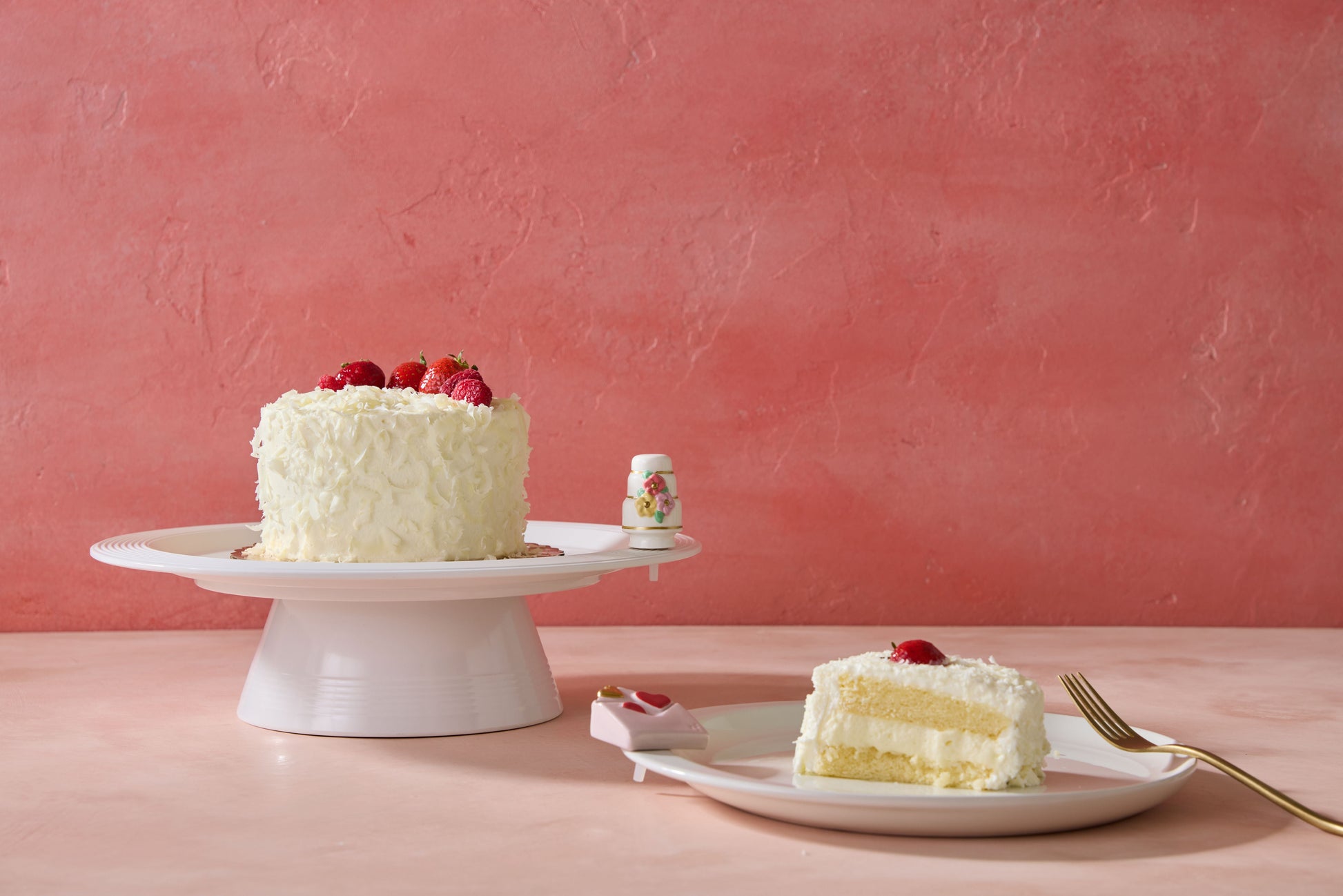 White cake with strawberries on a platter with nora fleming minis, on a pink background