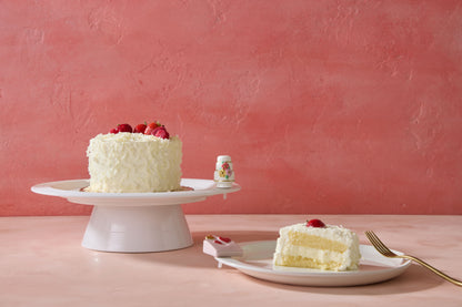 White cake with strawberries on a platter with nora fleming minis, on a pink background
