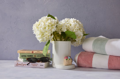 White flowers in a vase on books with a stack of towels and sunglasses on a gray surface.