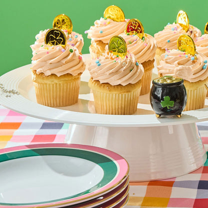Black pot with a green clover mini on a white surface with cupcakes against a  green background and plaid tablecloth