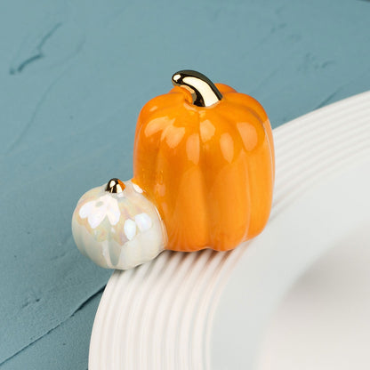 Two ceramic pumpkins, one orange and one white mini, on a white plate against a teal background.