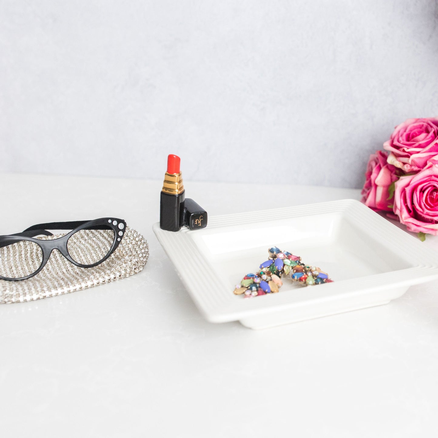 red lipstick and square napkin holder with pink roses and reading glasses