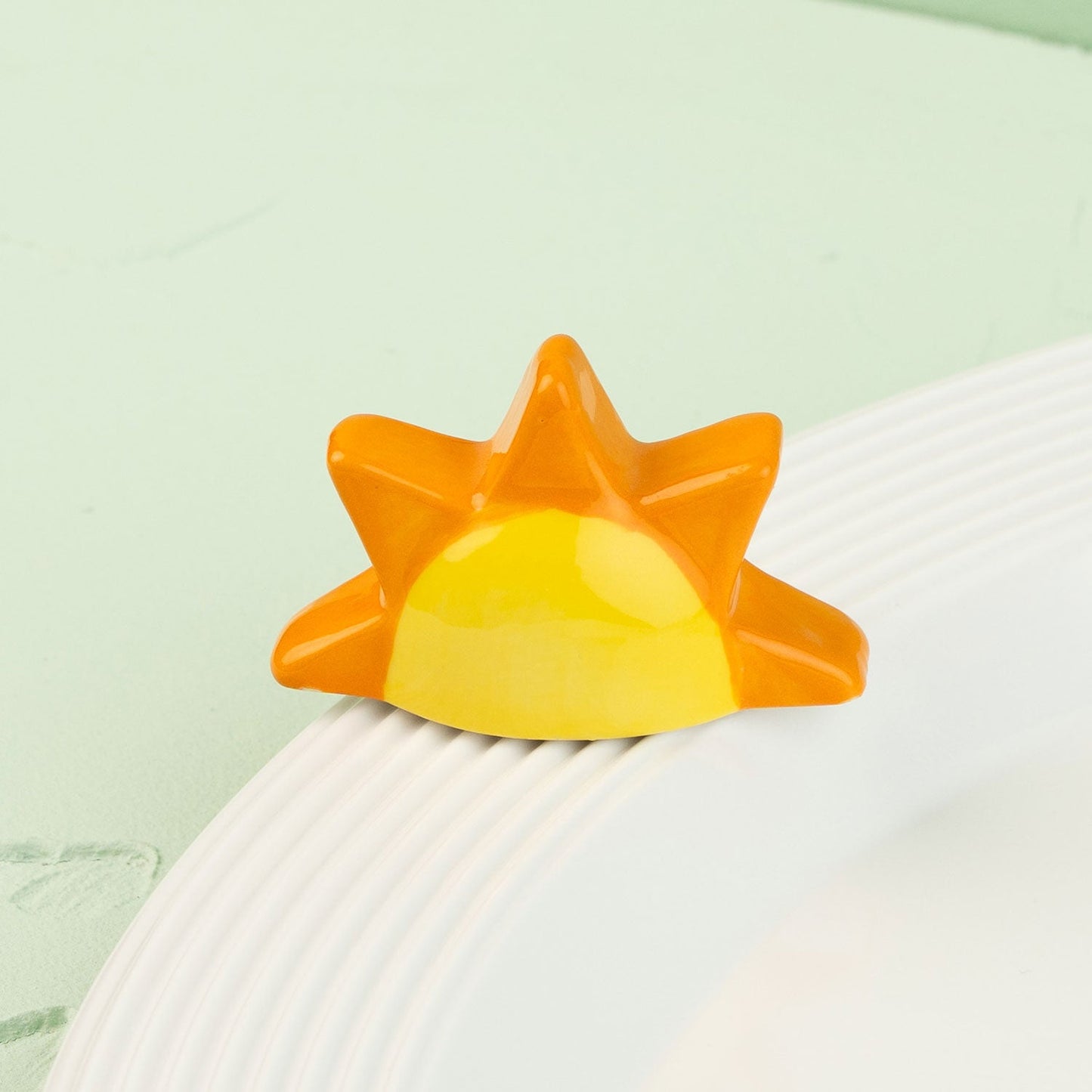 Sun-shaped mini with orange and yellow gradient on a white surface with a light green background